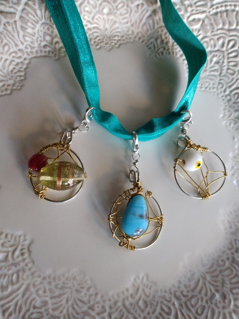 Three decorative goddess loc braid hair adornment pendants on a turquoise ribbon against a textured white background